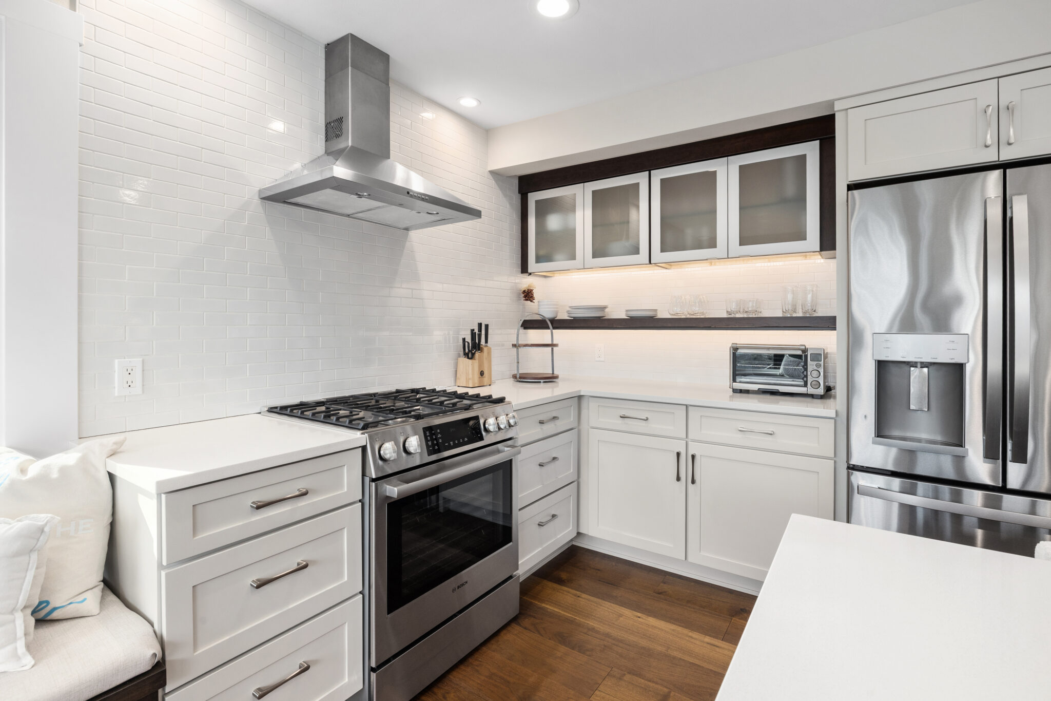 White kitchen with subway tile backsplash, stainless gas range and hood, and glass-front cabinets over open shelving