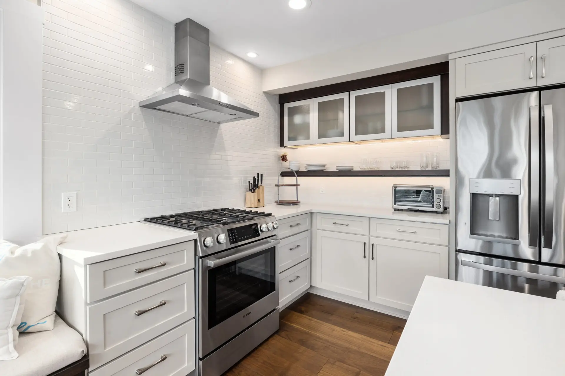 White kitchen with subway tile backsplash, stainless gas range and hood, and glass-front cabinets over open shelving