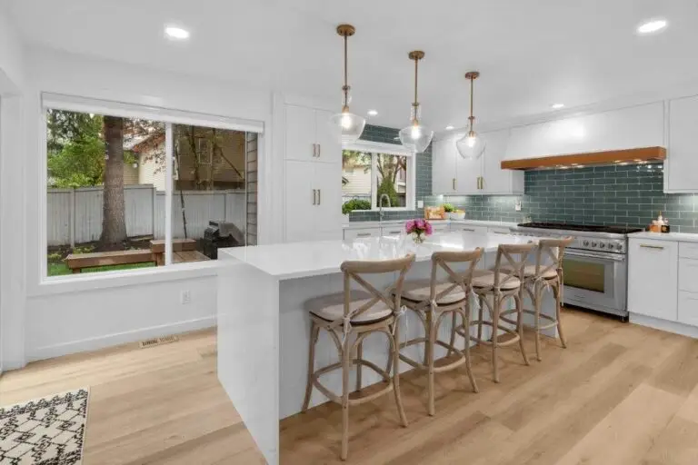 Coastal white kitchen with teal subway tile backsplash, quartz waterfall island and wood cross-back bar stools