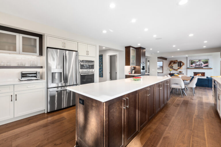 Long dark wood kitchen island with white quartz countertop, stainless appliances, and open flow to the living room