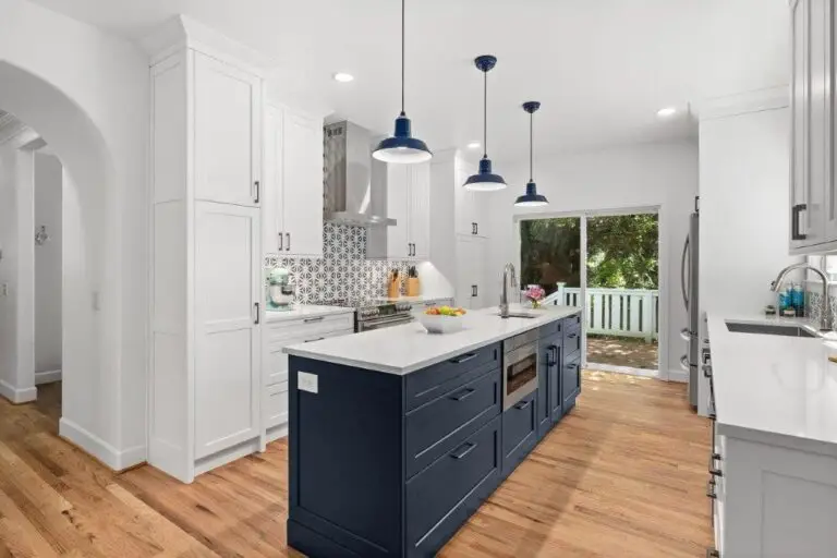 Kitchen with navy island, white quartz counters, blue pendant lights, patterned backsplash and arched doorway