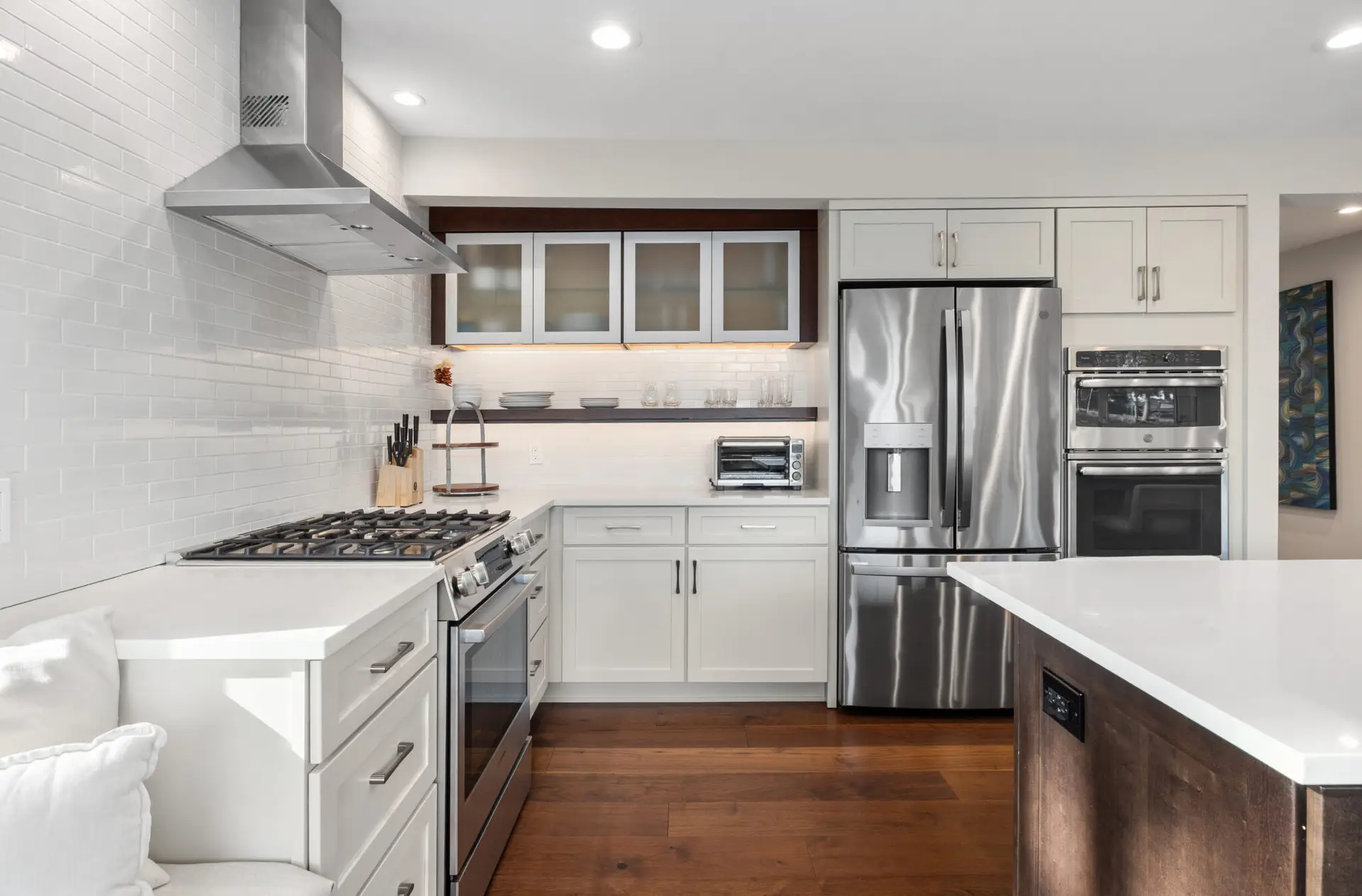 White shaker kitchen with stainless fridge, double wall ovens, gas range, and dark wood accent shelving