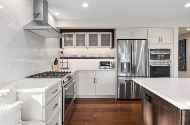 White shaker kitchen with stainless fridge, double wall ovens, gas range, and dark wood accent shelving