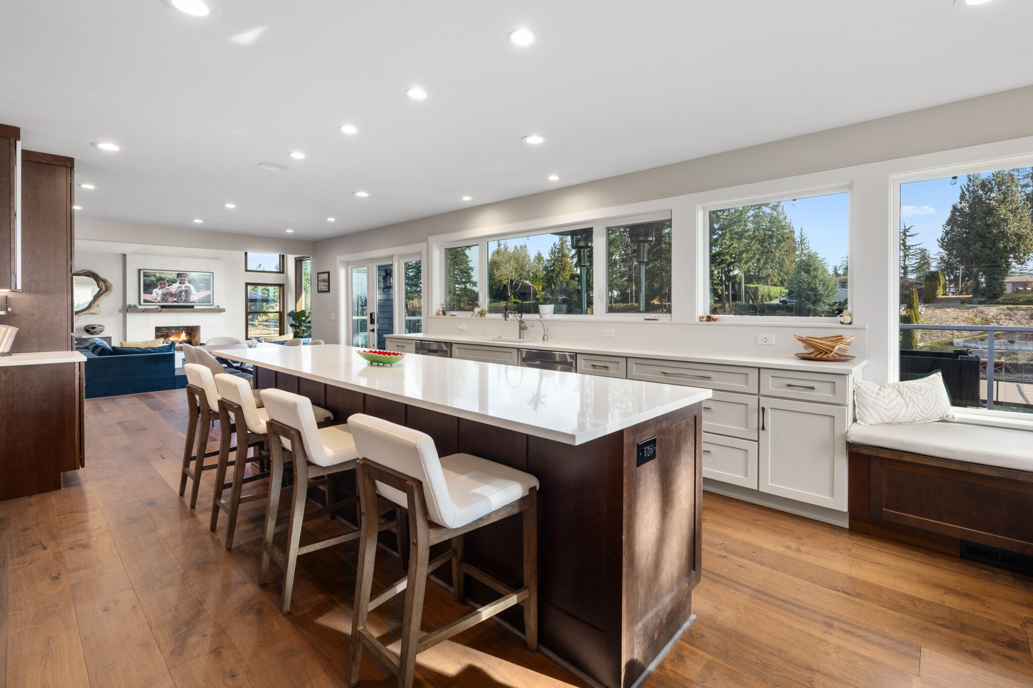 Oversized quartz-topped island with upholstered bar stools and a wall of windows in a lakeside kitchen remodel