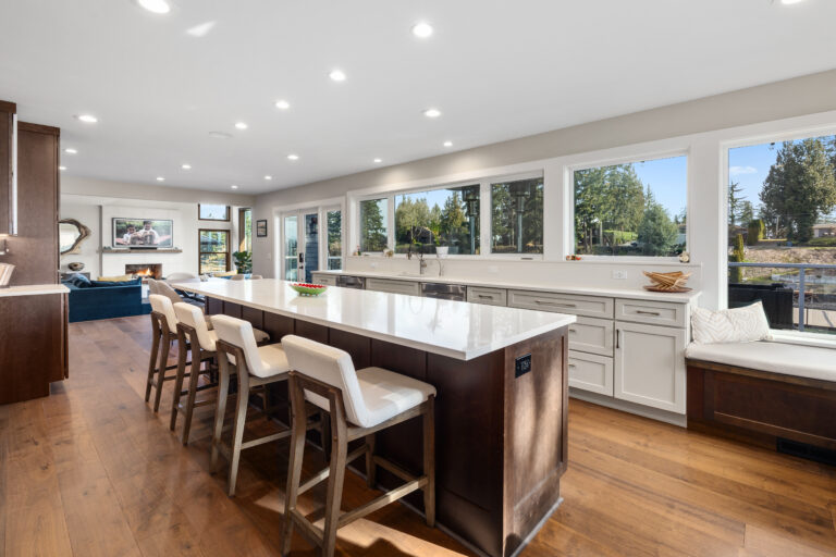 Oversized quartz-topped island with upholstered bar stools and a wall of windows in a lakeside kitchen remodel