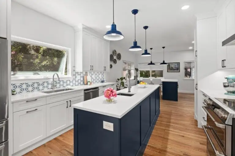 Long navy island with white quartz top, blue barn pendants, white perimeter cabinets and patterned tile backsplash