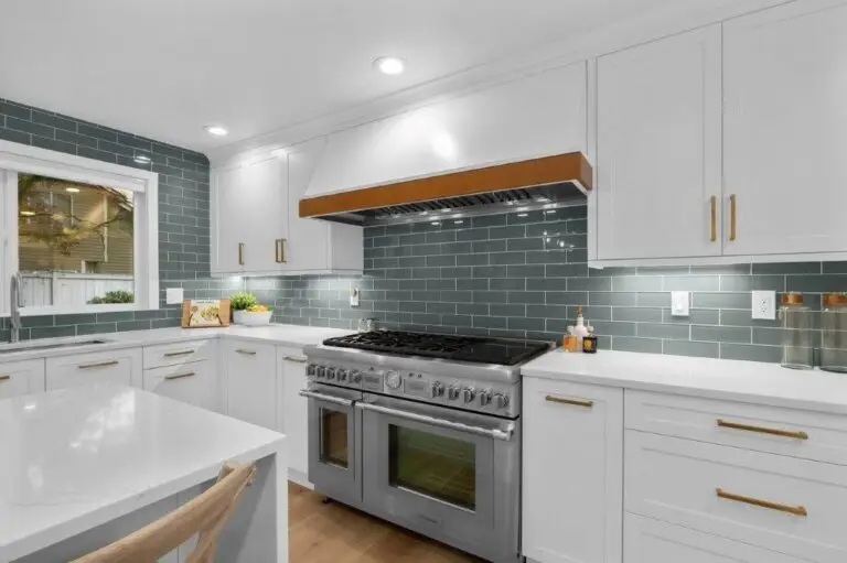 Professional stainless range under white hood with wood trim, teal glass subway tile backsplash and brass hardware