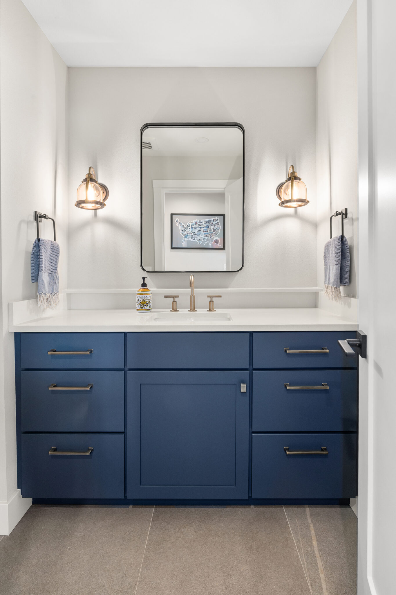 Navy blue bathroom vanity with white quartz countertop, brass hardware, sconces, and black-framed mirror