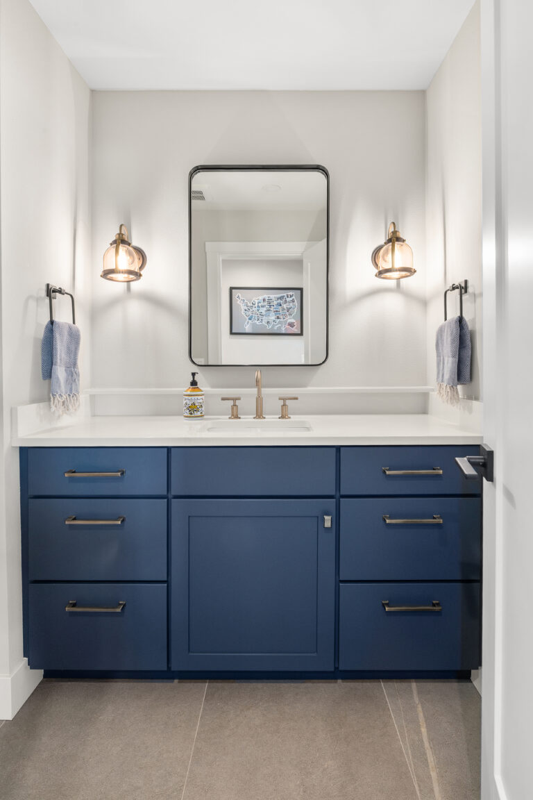 Navy blue bathroom vanity with white quartz countertop, brass hardware, sconces, and black-framed mirror