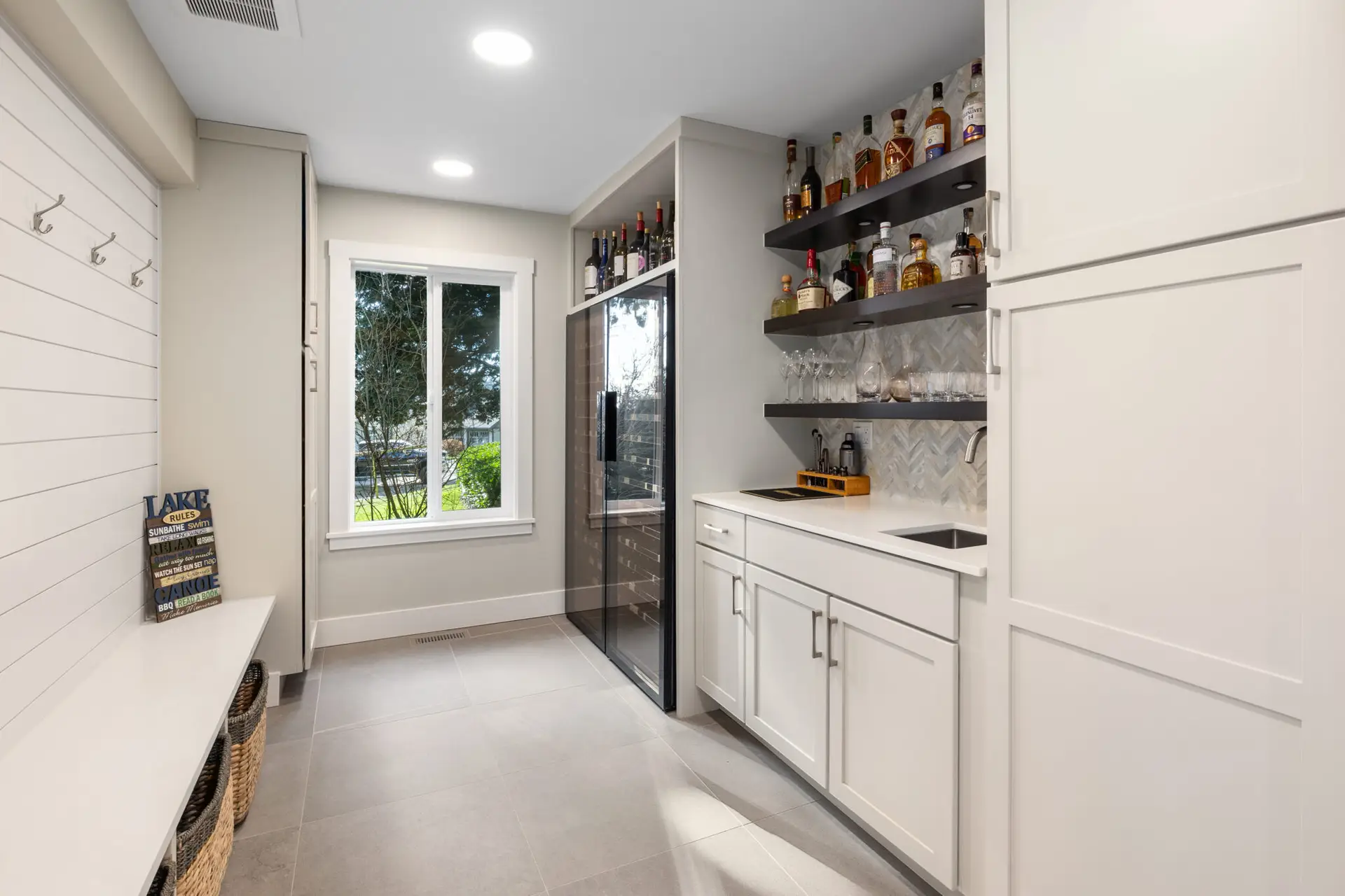 Mudroom and bar area with shiplap coat wall, wine fridge, and floating shelves of spirits over white cabinets