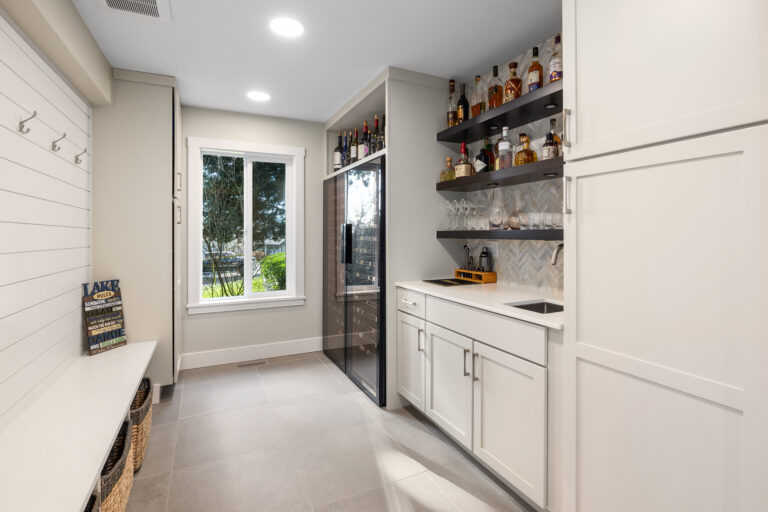 Mudroom and bar area with shiplap coat wall, wine fridge, and floating shelves of spirits over white cabinets