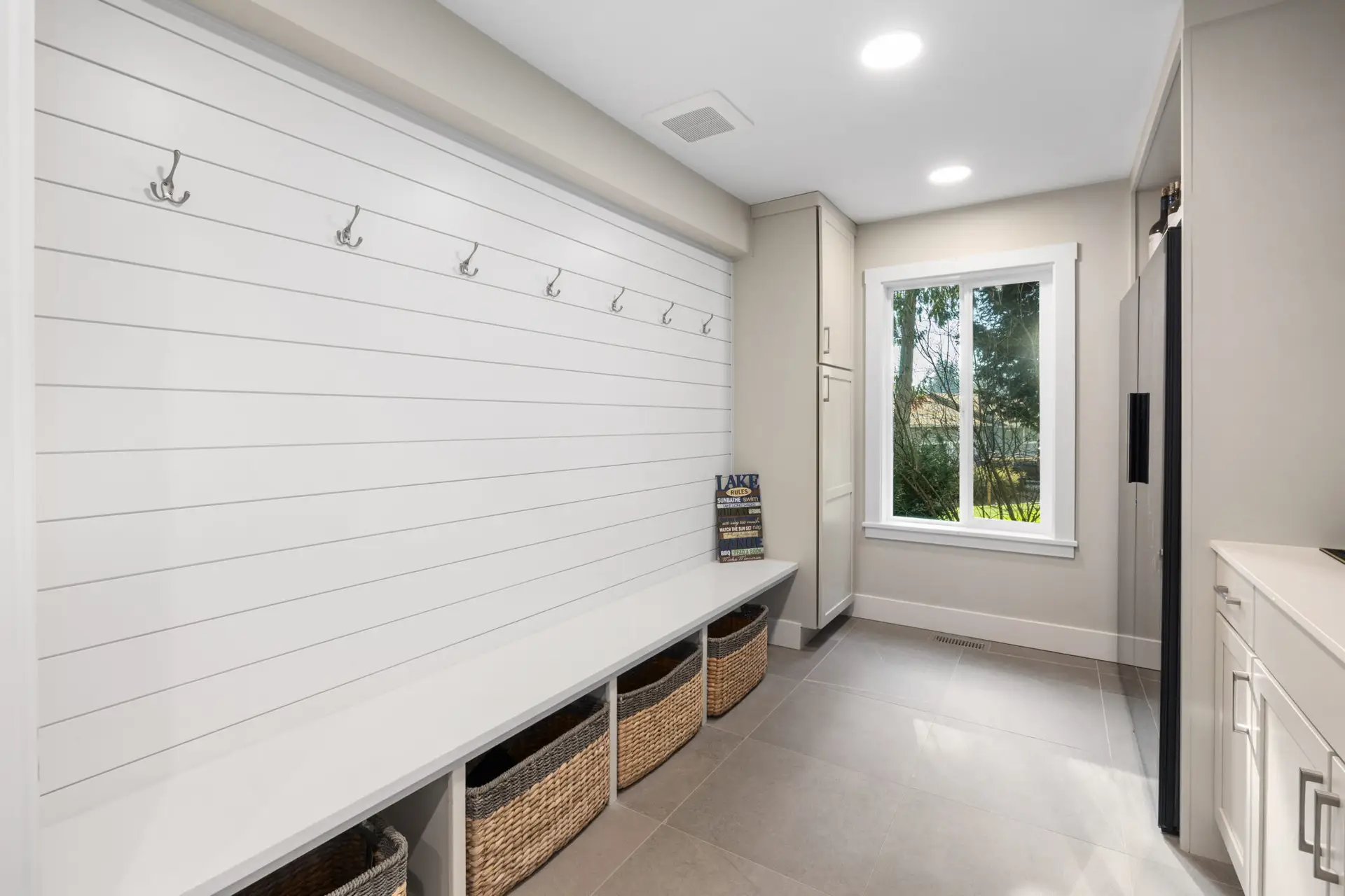 Bright mudroom with white shiplap wall, coat hooks, built-in bench, and woven storage baskets