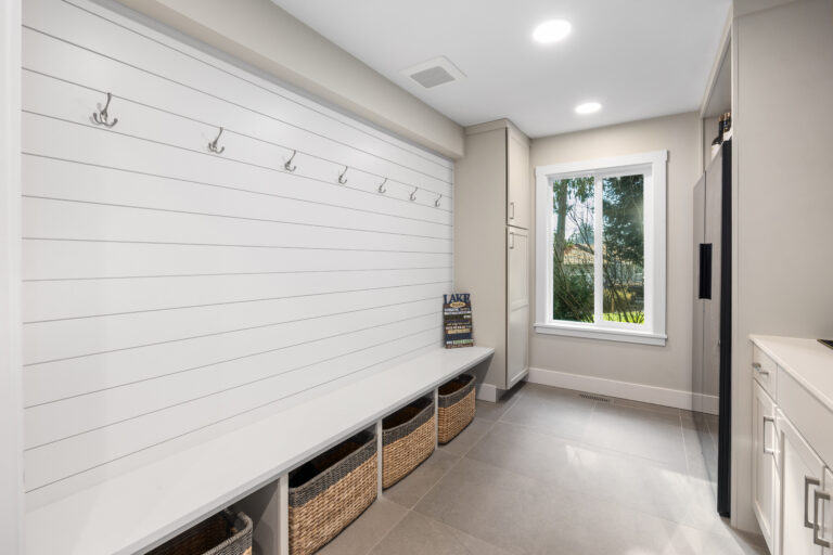 Bright mudroom with white shiplap wall, coat hooks, built-in bench, and woven storage baskets