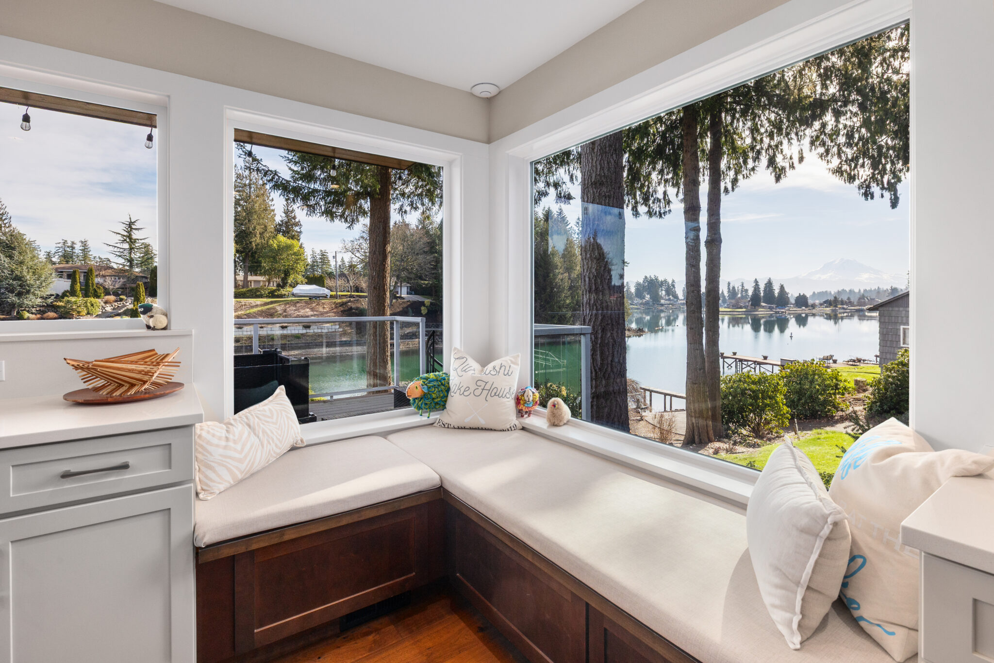 L-shaped window seat with pillows overlooking the lake, dock, and evergreens at a lakeside remodel