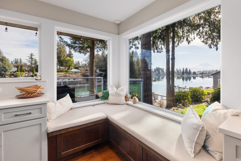 L-shaped window seat with pillows overlooking the lake, dock, and evergreens at a lakeside remodel