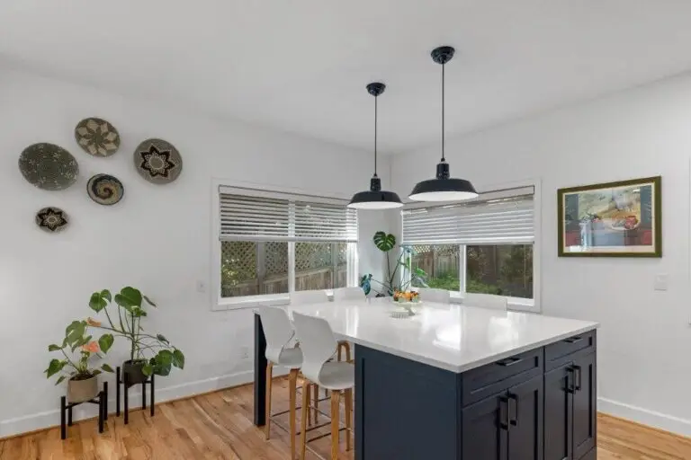 Dining nook with white quartz table extending from a navy island, white chairs, black pendants and woven baskets