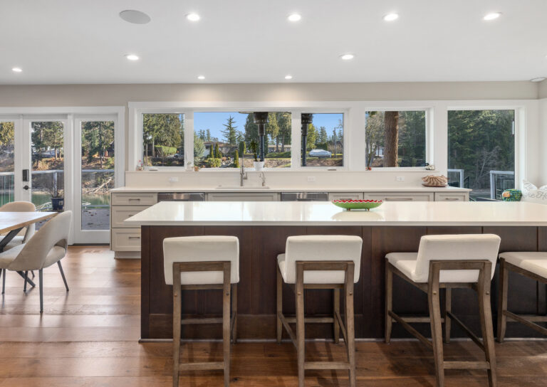 Kitchen island with cream upholstered bar stools, quartz counters, and lakeside windows above the sink wall