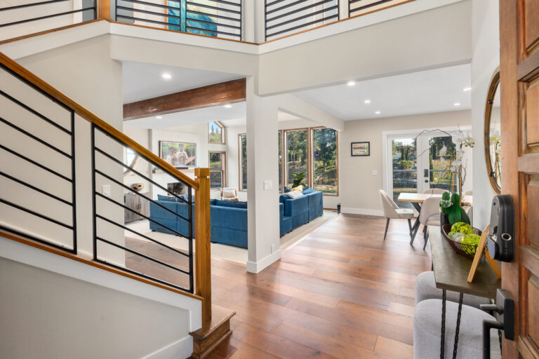 Two-story foyer with wood and iron staircase opening to a living room with blue sectional and lake views