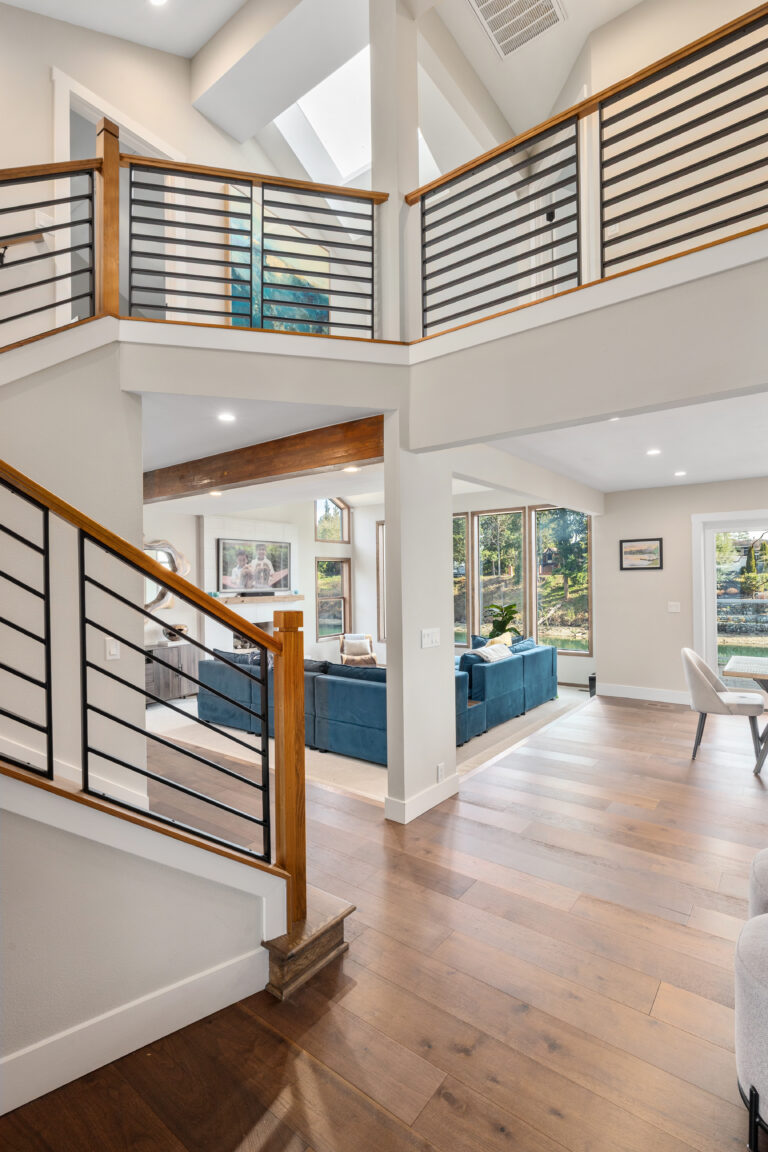 Open staircase with horizontal iron railings, exposed wood beam, and sightlines to the lakeside living room