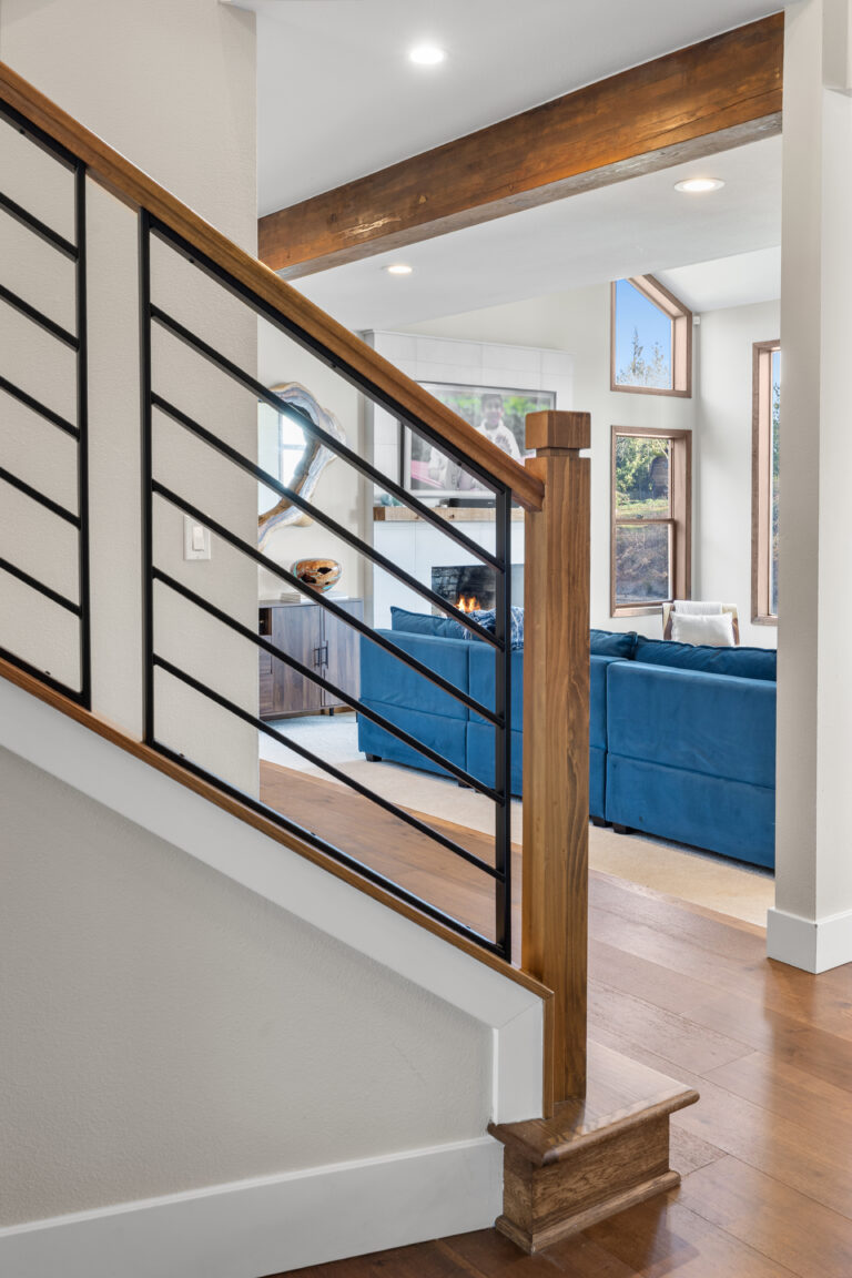 Stair railing detail with warm wood posts and black metal balusters beside a blue velvet sectional