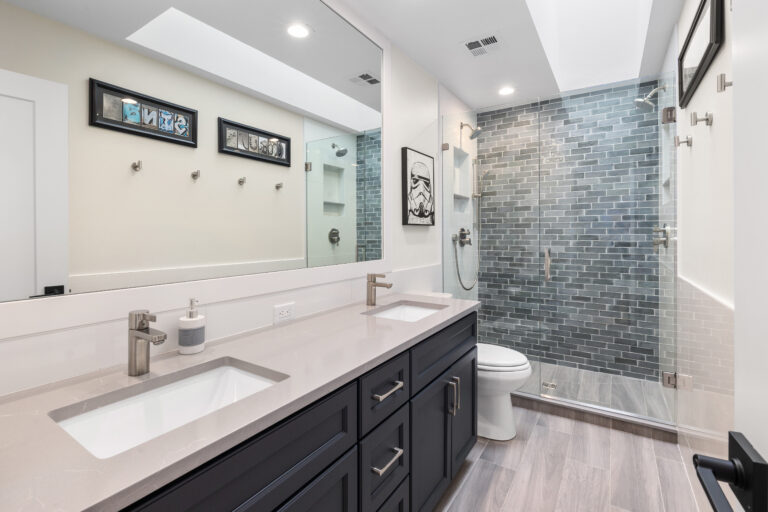 Bathroom with dark blue double vanity, gray quartz top, and glass shower with blue-gray subway tile