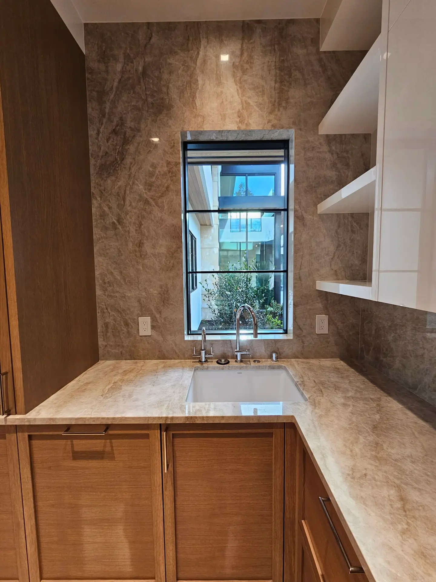 Full-height quartzite backsplash wrapping the pantry sink window, with oak cabinetry below