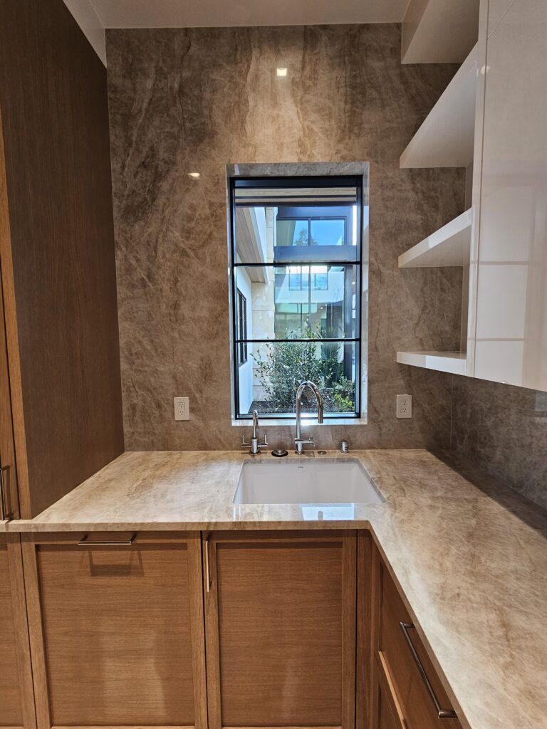 Full-height quartzite backsplash wrapping the pantry sink window, with oak cabinetry below