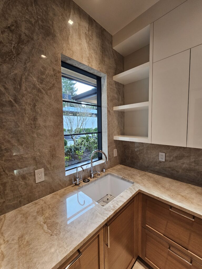 Quartzite countertop with undermount sink and polished chrome faucets beneath a black-framed window