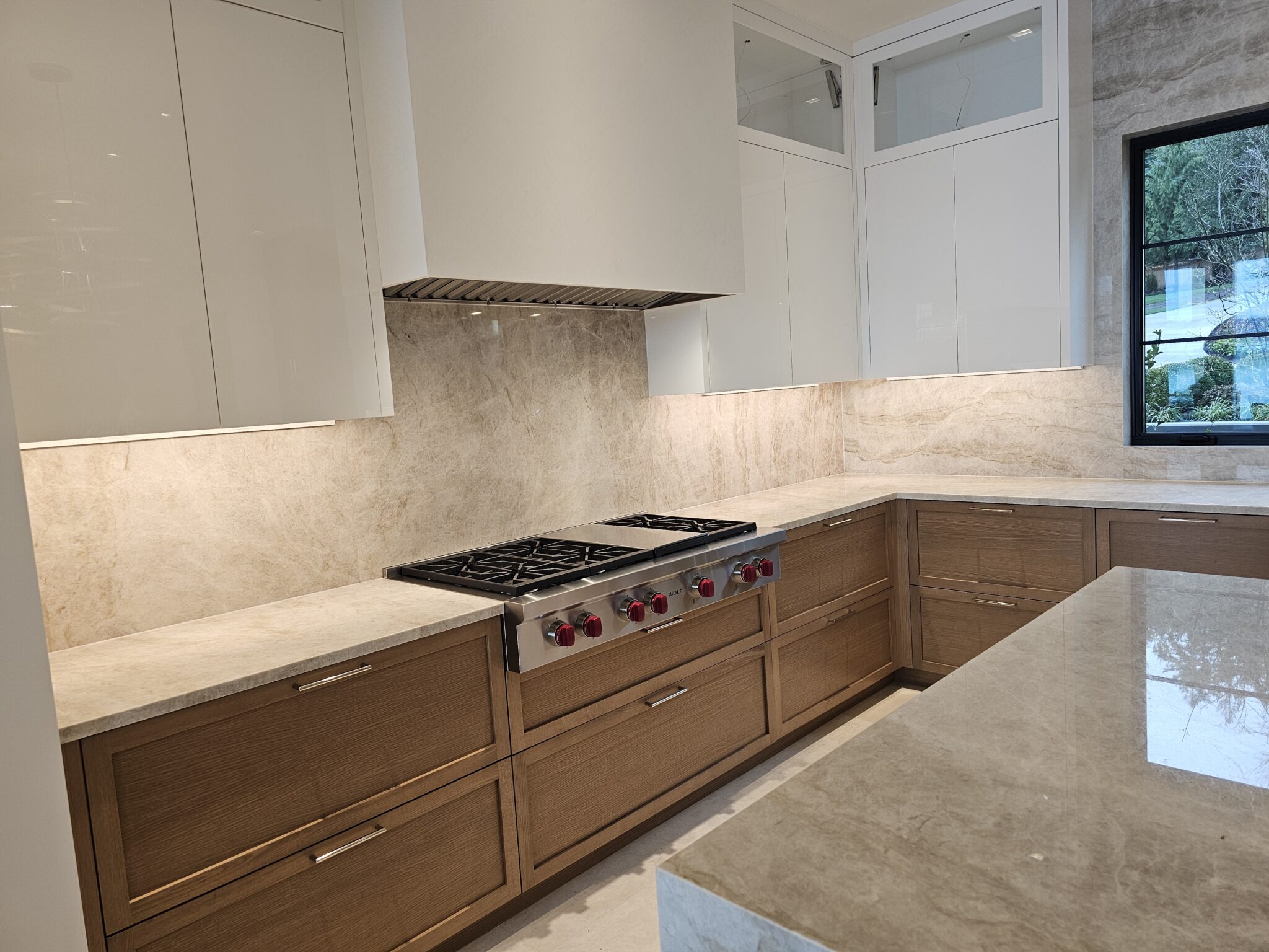 Professional gas rangetop set into quartzite counters with full-height slab backsplash and white hood