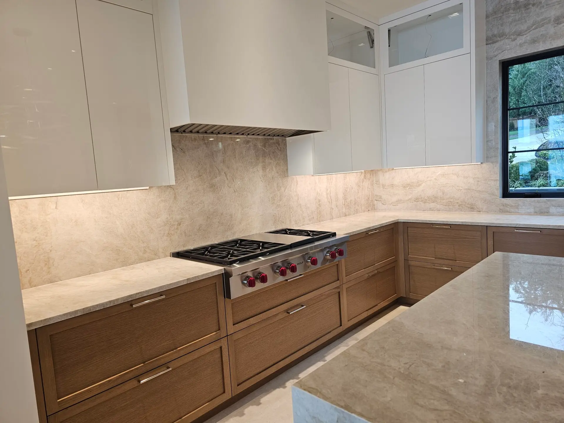 Professional gas rangetop set into quartzite counters with full-height slab backsplash and white hood