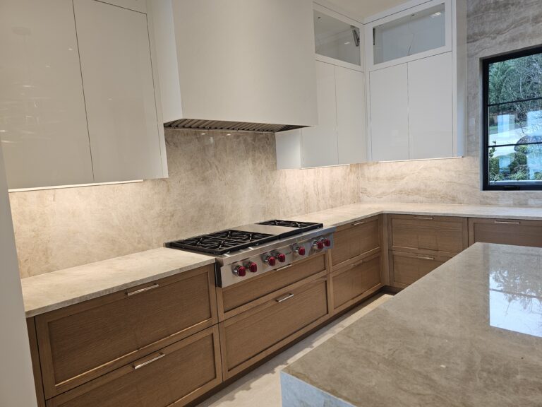Professional gas rangetop set into quartzite counters with full-height slab backsplash and white hood