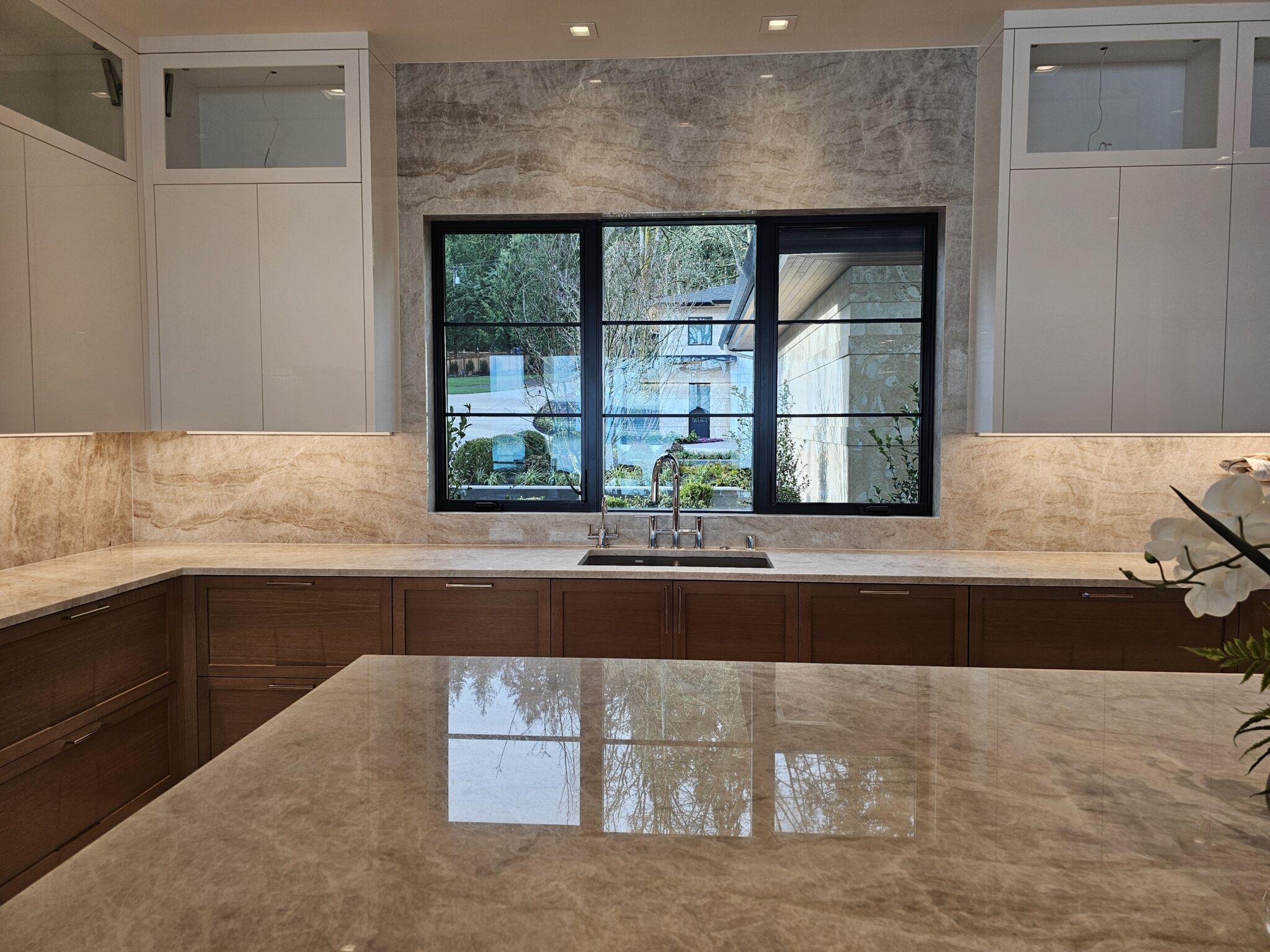 Kitchen sink wall with black-framed windows and taupe quartzite counters and backsplash