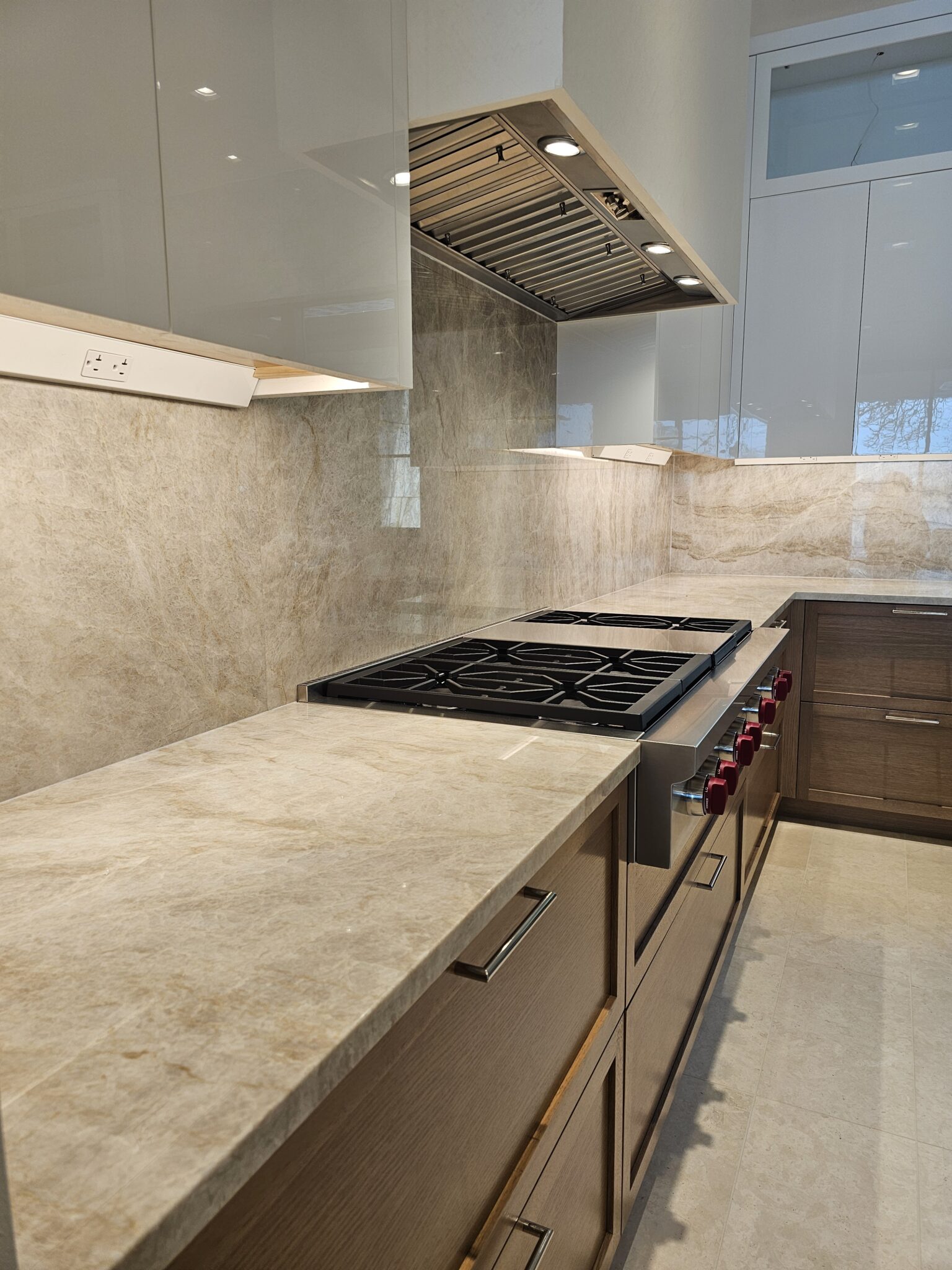 White plaster range hood over the gas rangetop, seen past the quartzite island waterfall edge