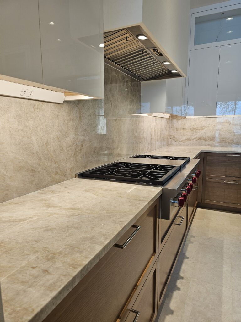 White plaster range hood over the gas rangetop, seen past the quartzite island waterfall edge