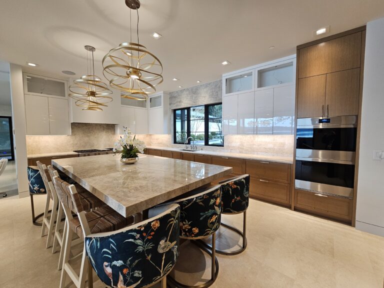Wide kitchen view showing the quartzite island, wall ovens in oak cabinetry, and floral counter stools