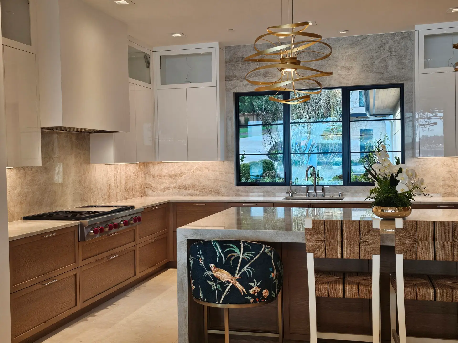 Corner of the quartzite island with a floral stool, gold pendant, and rangetop wall behind