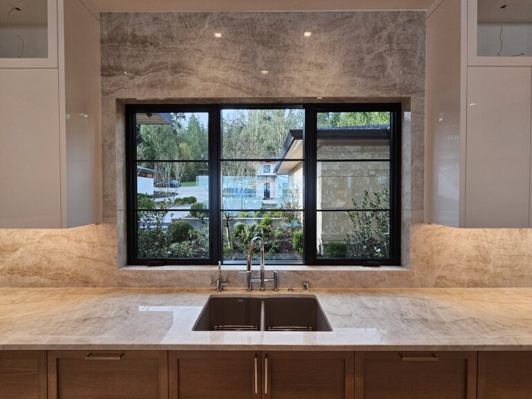 Straight-on view of the sink window framed in taupe quartzite slab with oak cabinets