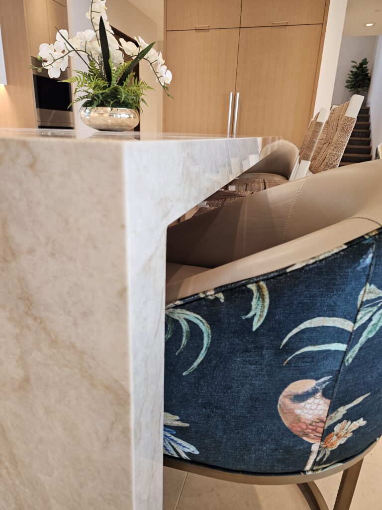 Close-up of the island quartzite waterfall corner with a floral counter stool and orchid