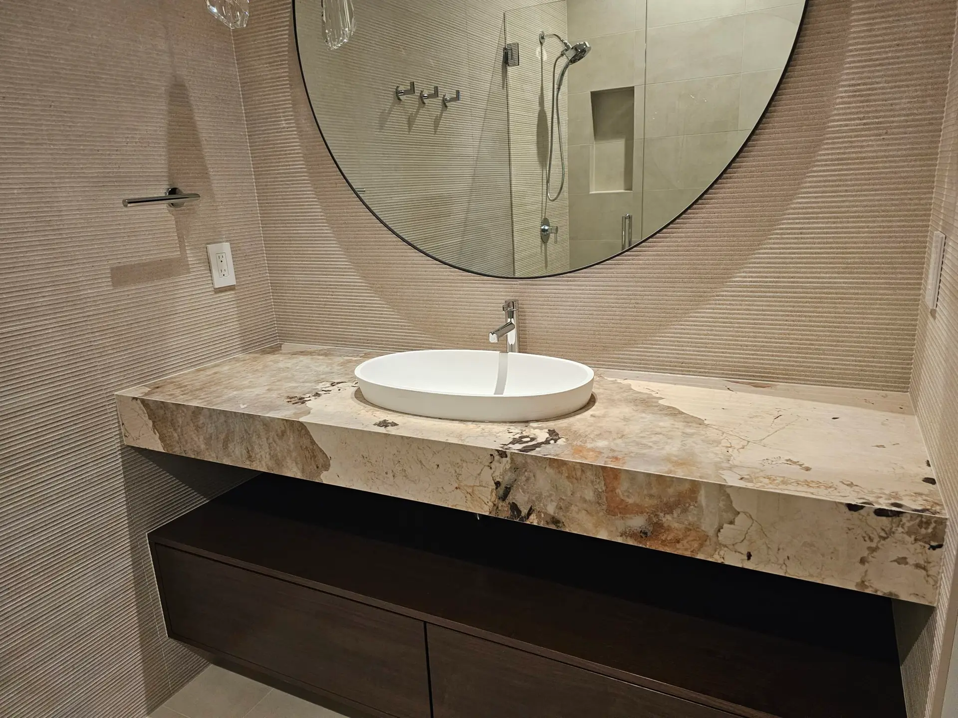 Floating vanity in dramatic bold-veined stone with white vessel sink and round backlit mirror
