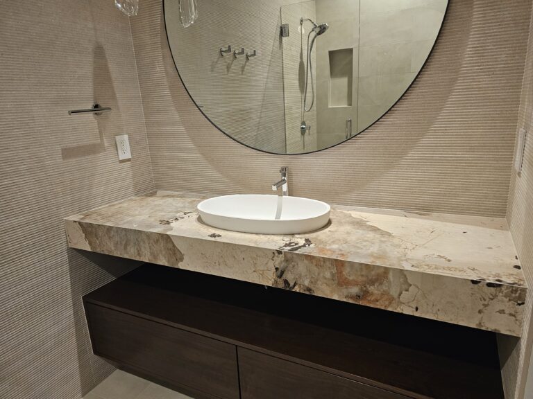Floating vanity in dramatic bold-veined stone with white vessel sink and round backlit mirror