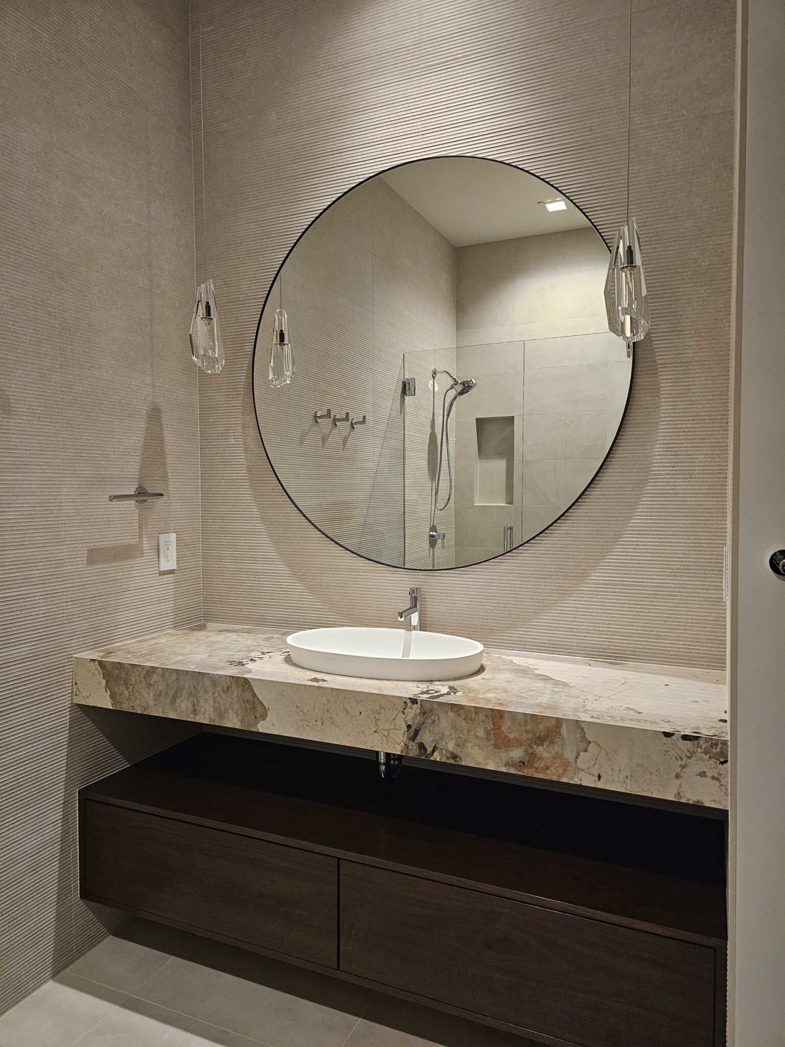 Round mirror and wall-mounted faucet over a vessel sink on a bold-veined stone vanity
