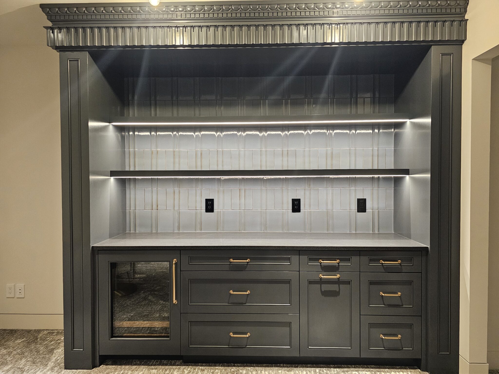 Charcoal bar cabinetry with beverage fridge, gray quartz counter, and backlit tile niche