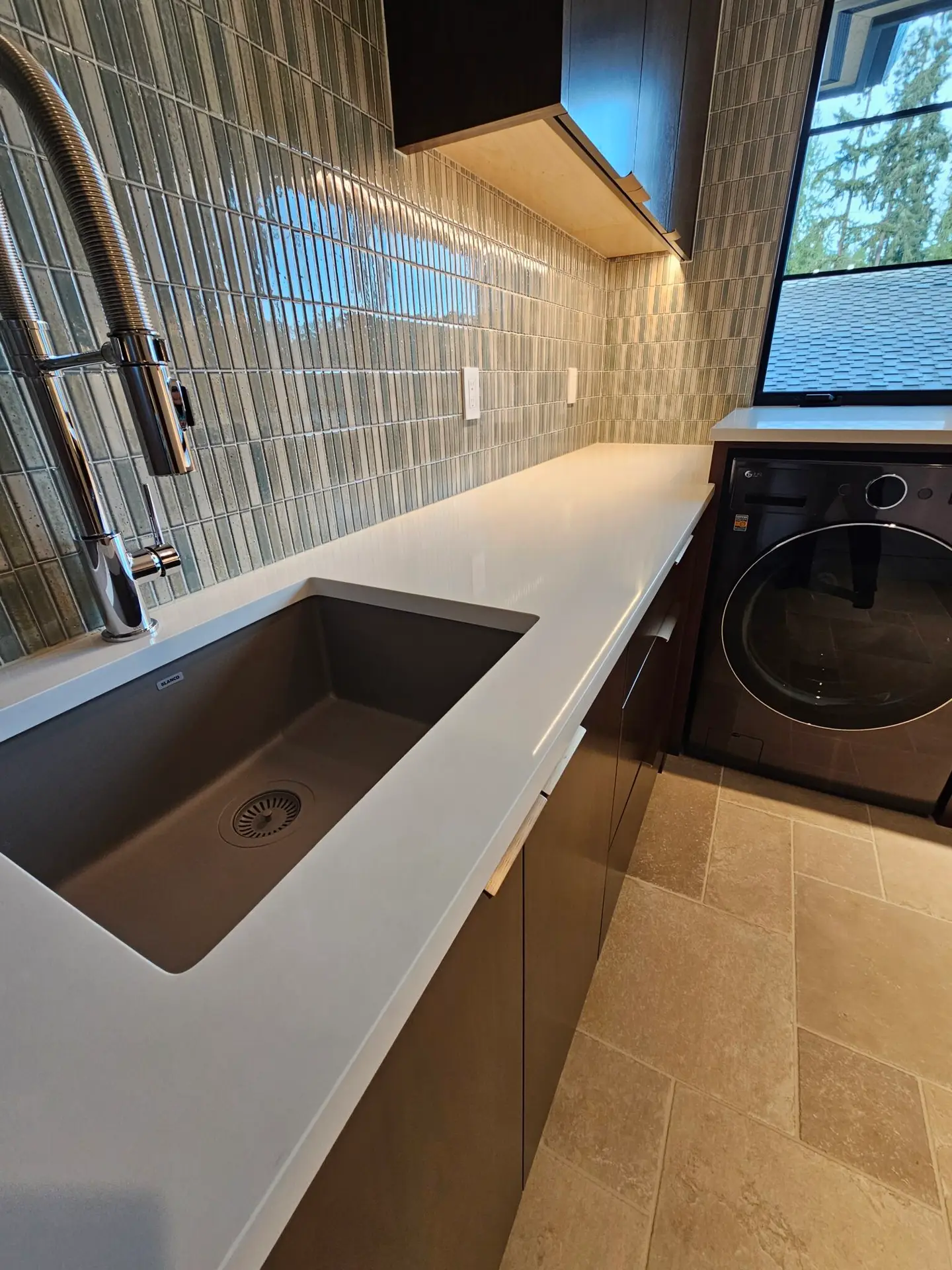 Laundry sink set in white quartz countertop against a glossy green mosaic tile wall