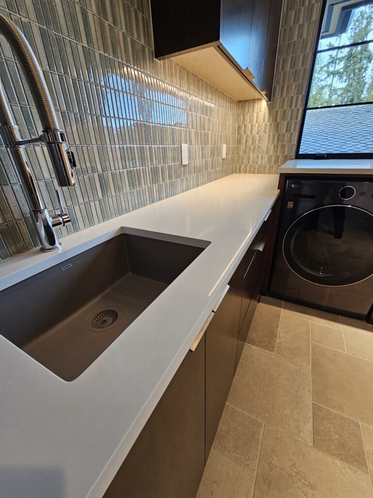 Laundry sink set in white quartz countertop against a glossy green mosaic tile wall