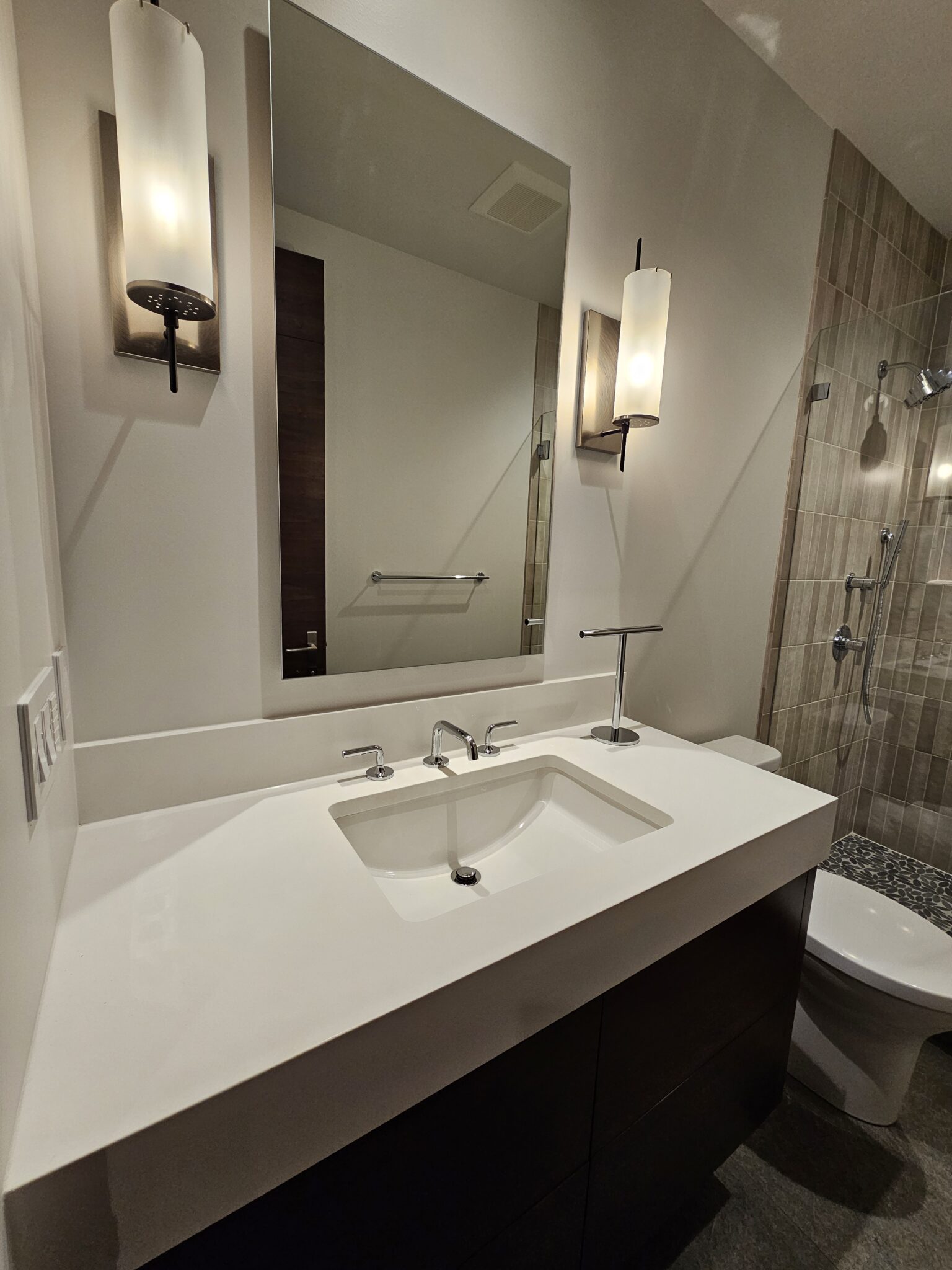 Guest bath with white quartz vanity, cylinder sconces, and tiled walk-in shower beyond