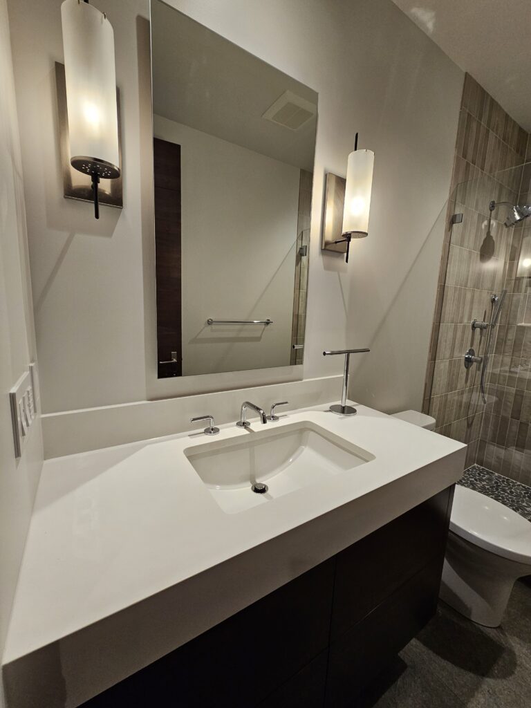 Guest bath with white quartz vanity, cylinder sconces, and tiled walk-in shower beyond