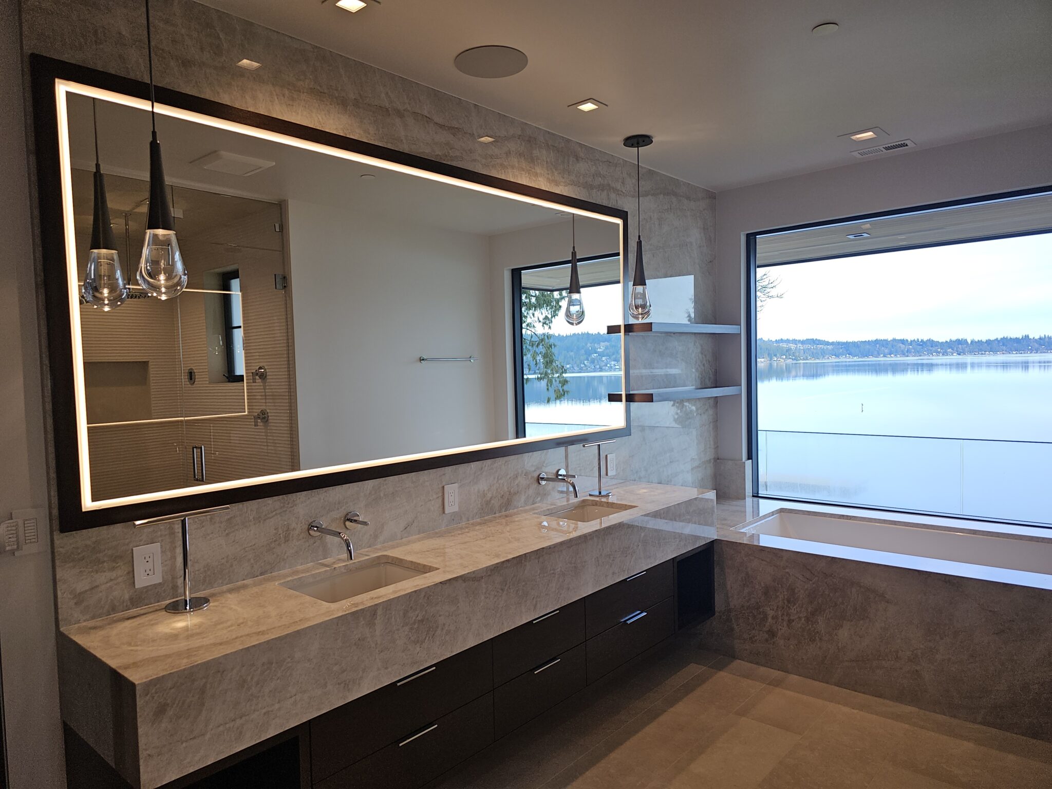 Primary bath with taupe quartzite floating vanity, backlit mirror, and tub at the lake-view window