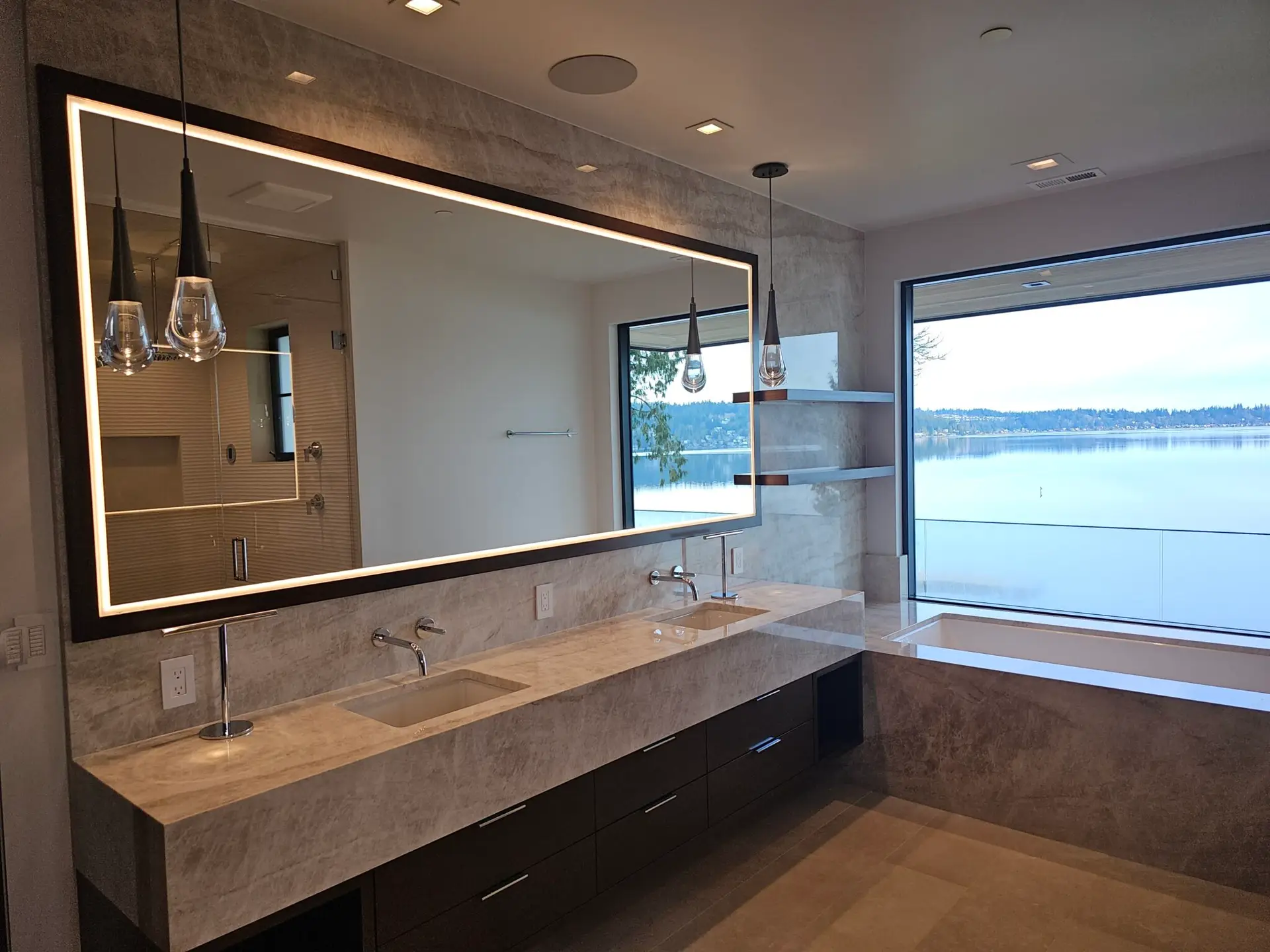 Primary bath with taupe quartzite floating vanity, backlit mirror, and tub at the lake-view window