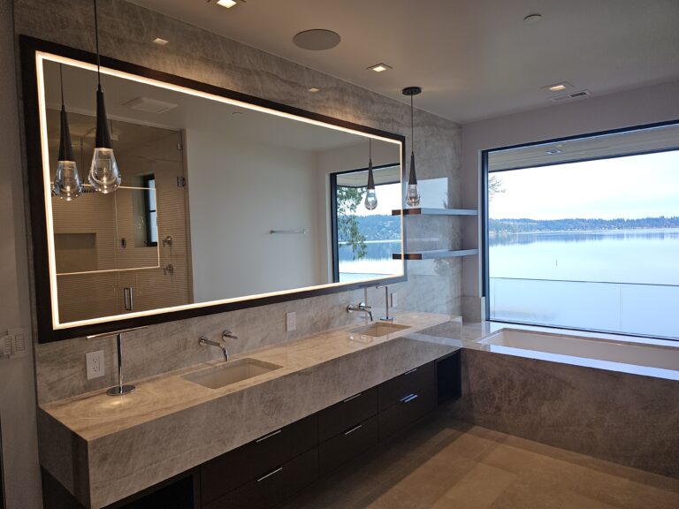 Primary bath with taupe quartzite floating vanity, backlit mirror, and tub at the lake-view window