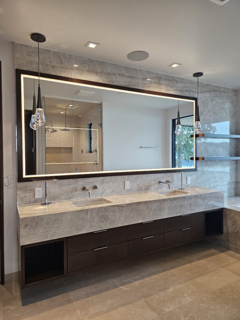 Backlit mirror and quartzite vanity wall in the primary bath with skylight overhead